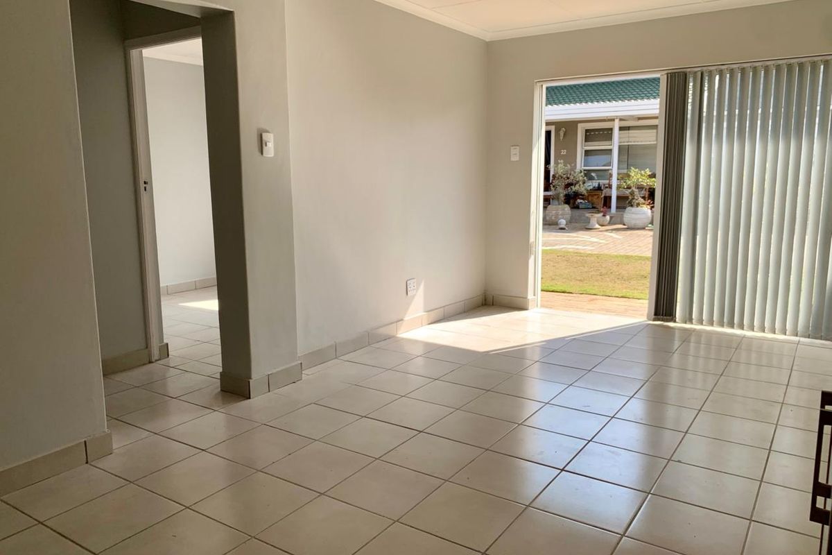 An empty, neutrally painted living room featuring ceramic floor tiles and a sliding glass door providing access to an outdoor patio area.