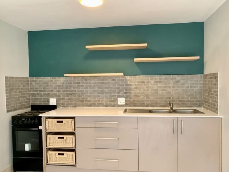 A modern kitchen featuring sleek cabinetry, a subway tile backsplash, floating shelves, and a built-in stove with a clean, contemporary finish.