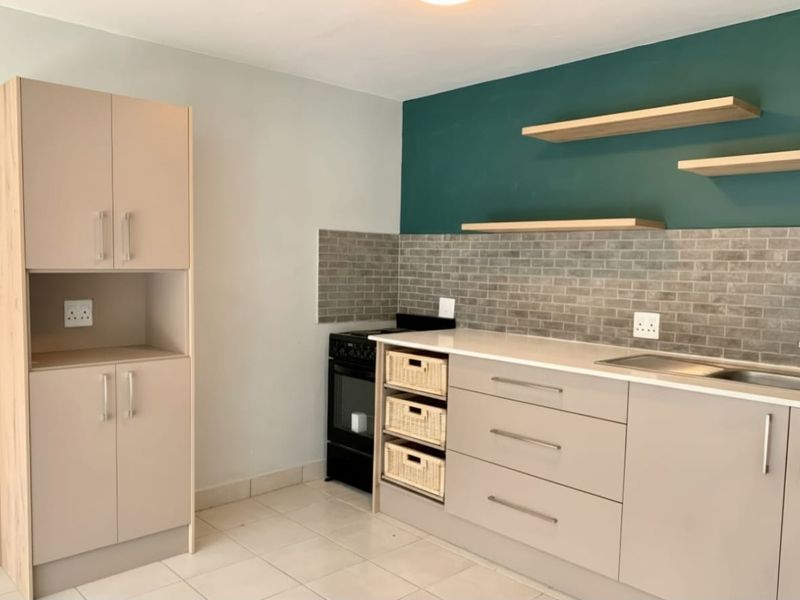 Modern kitchen featuring neutral cabinetry, stone countertops, a tiled backsplash, floating shelves, and a freestanding stove.