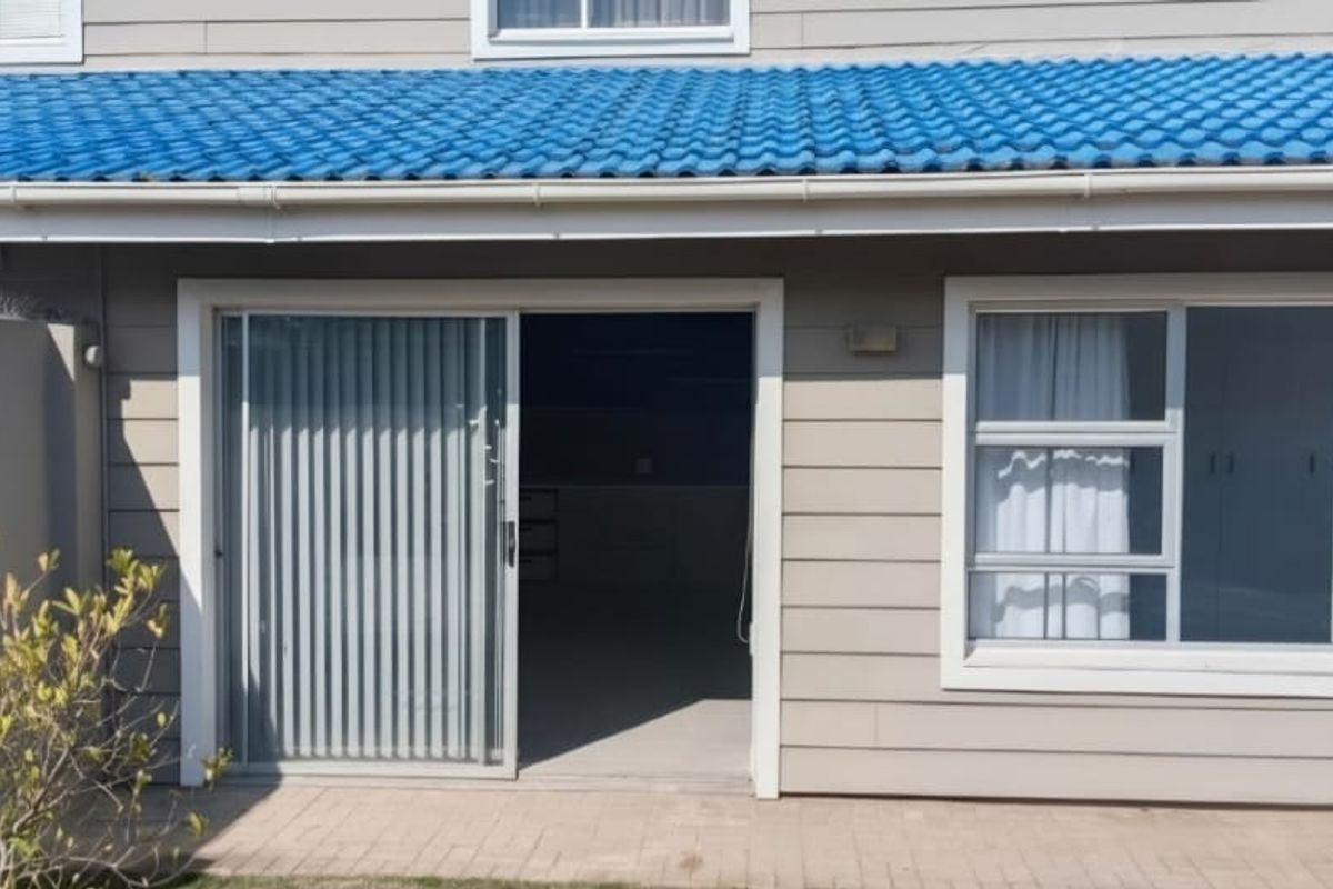 Rear exterior view of the apartment featuring a paved patio, sliding glass door access, and blue tiled roofing.