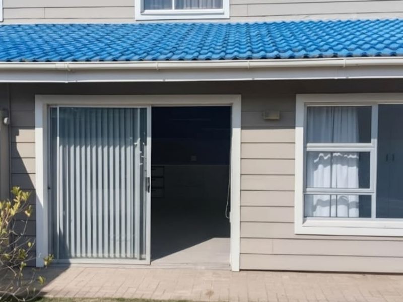 Rear exterior view of the apartment featuring a paved patio, sliding glass door access, and blue tiled roofing.