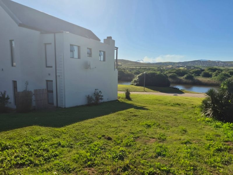 Rear view of a white residential property featuring a pitched roof and chimney, overlooking a grassy lawn and natural landscape.