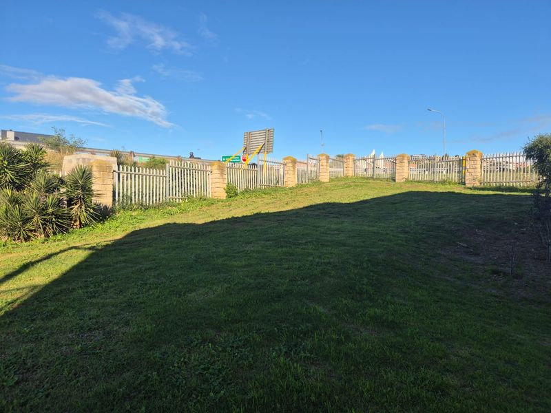 A vacant residential plot featuring a grassed area enclosed by perimeter fencing with brick pillars and a metal security gate.