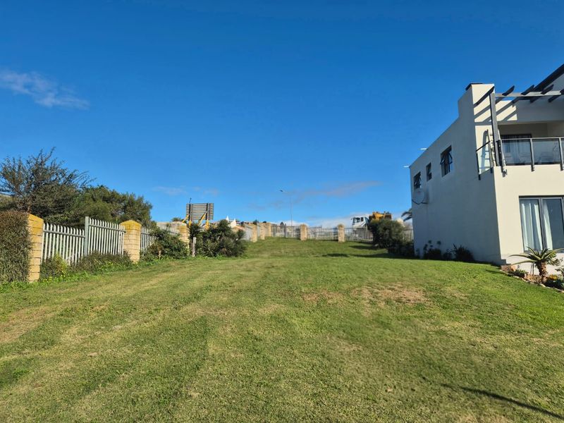 A spacious, well-maintained grassy backyard area featuring perimeter fencing and a view of the adjacent residential structure.