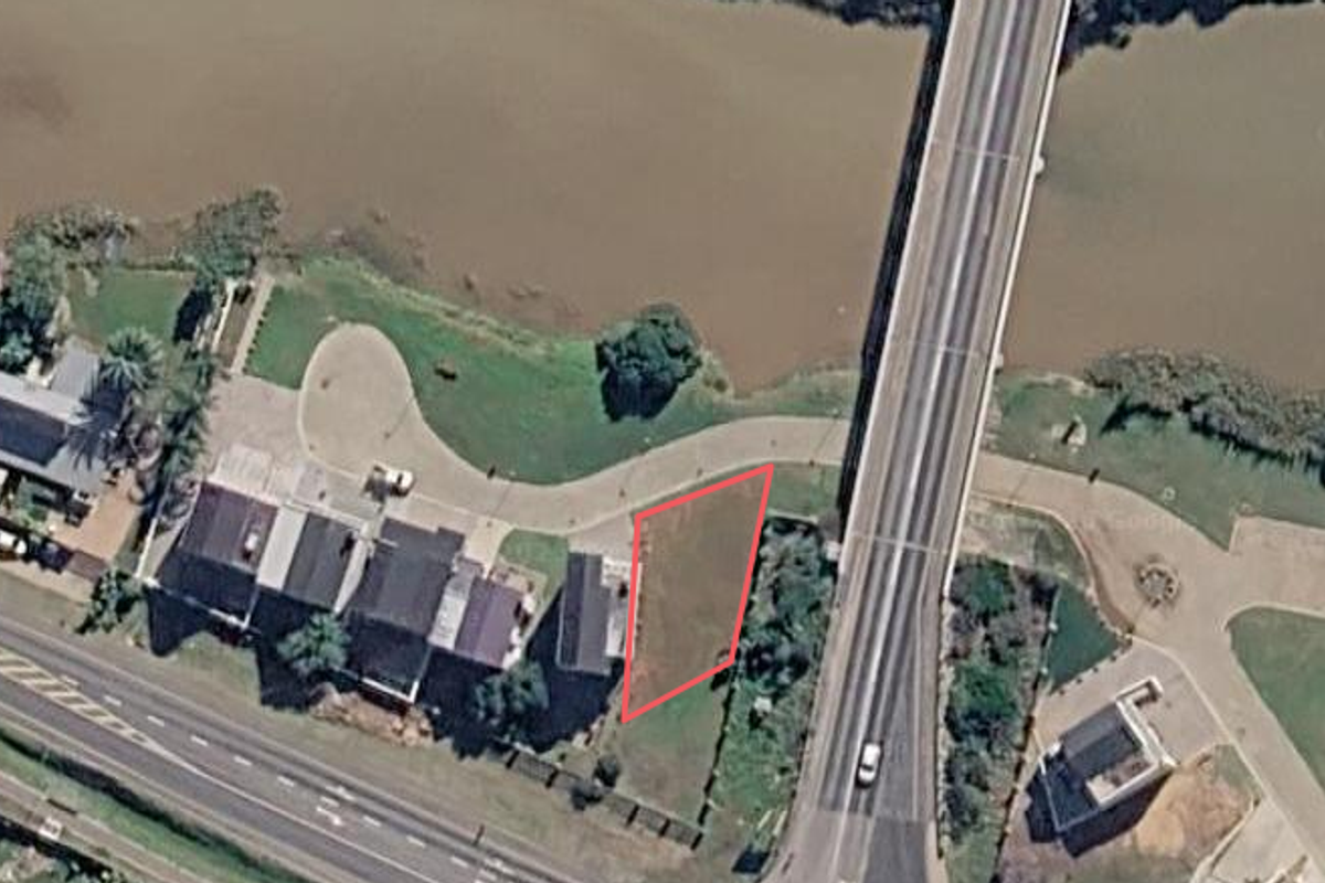 Aerial view of a vacant residential plot situated along the riverbank, adjacent to a bridge and established residential properties.