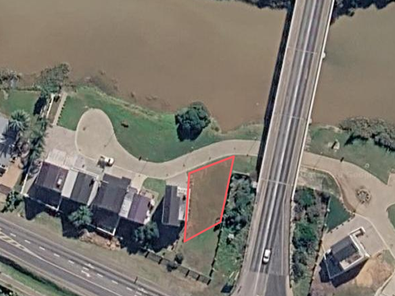 Aerial view of a vacant residential plot situated along the riverbank, adjacent to a bridge and established residential properties.