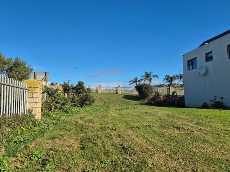 A spacious, grassed residential plot featuring perimeter steel fencing, stone masonry pillars, and a retaining wall, offering potential for development.