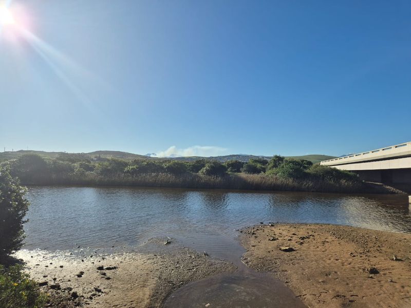 A scenic view of a river landscape featuring a bridge and natural vegetation under a clear blue sky.