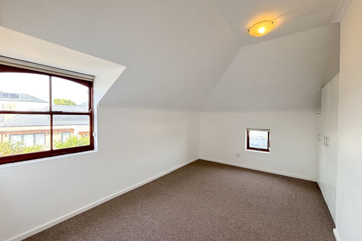 A bright, empty bedroom featuring a pitched ceiling, carpeted flooring, and built-in cupboards, offering a clean and versatile space.