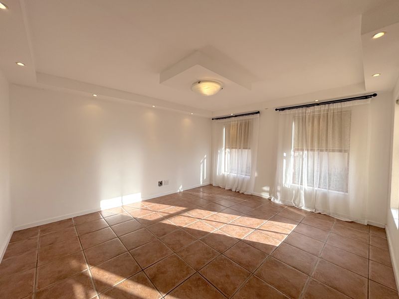 A bright, empty living room featuring neutral walls, ceramic tiled flooring, and recessed ceiling lighting, offering a versatile space for customization.