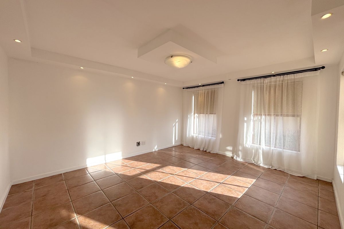 A bright, empty living room featuring neutral walls, ceramic tiled flooring, and recessed ceiling lighting, offering a versatile space for customization.
