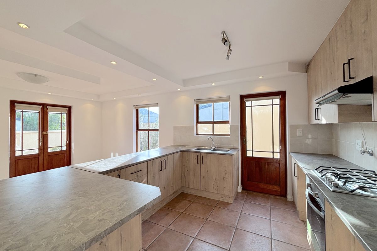 A bright, empty kitchen featuring wood-look cabinetry, laminate countertops, a gas hob, and tiled flooring with direct access to the exterior.
