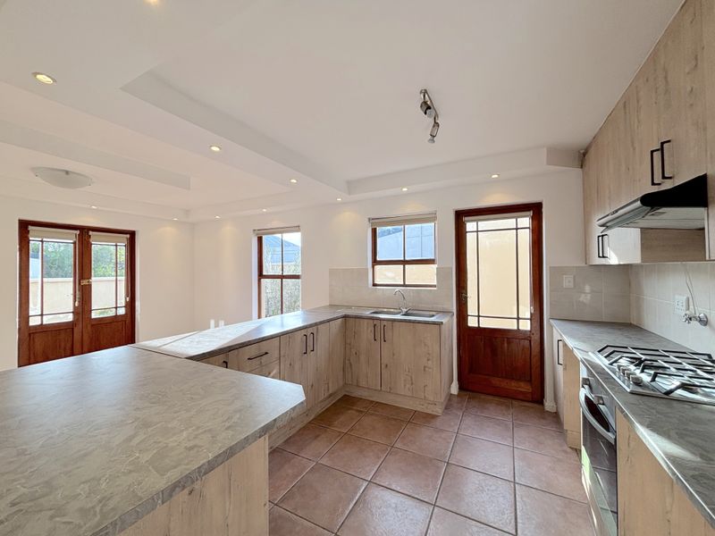 A bright, empty kitchen featuring wood-look cabinetry, laminate countertops, a gas hob, and tiled flooring with direct access to the exterior.