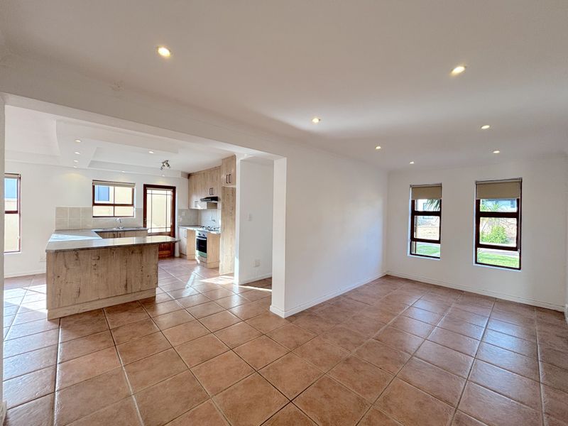 Spacious open-plan living and kitchen area featuring tiled flooring, modern cabinetry, built-in appliances, and ample natural light through multiple windows.
