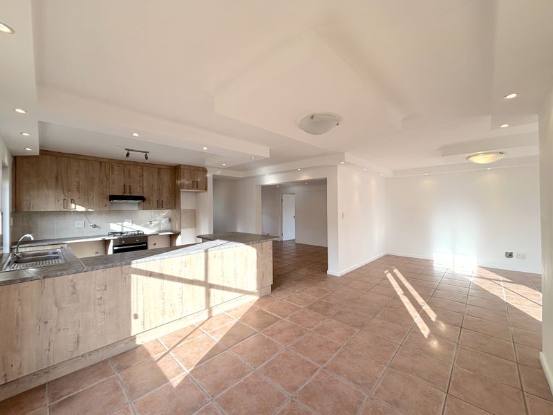 Spacious open-plan living area featuring a modern kitchen with wood-finish cabinetry, built-in appliances, and neutral ceramic floor tiles throughout.