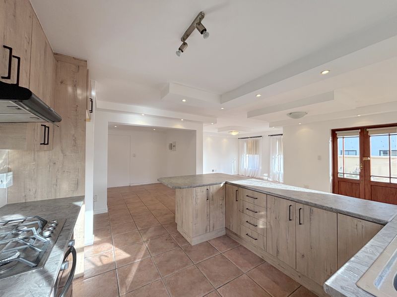 Spacious open-plan kitchen and living area featuring modern wood-look cabinetry, gas hob, tiled flooring, and recessed ceiling lighting with direct access to the exterior.