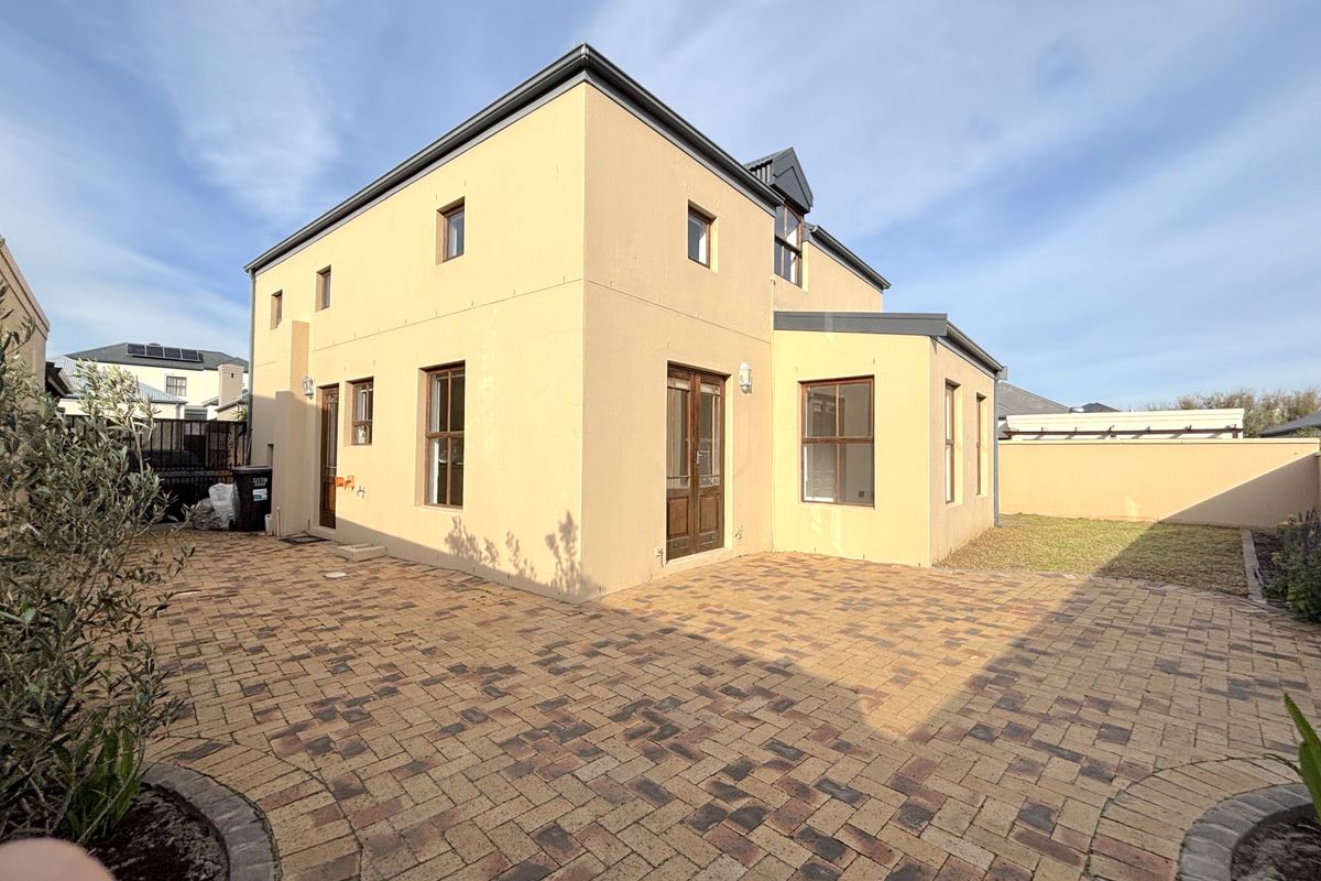 Rear view of the property featuring a paved patio area, plastered exterior walls, and timber-framed doors and windows.