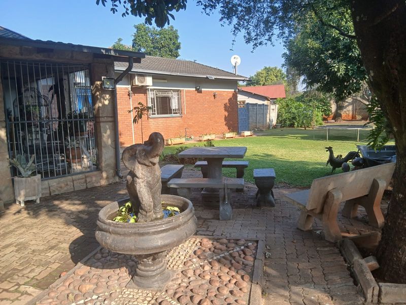Rear exterior view featuring a brick facade, paved patio area with a stone fountain, and established garden space.