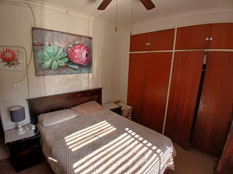 A bedroom featuring built-in wooden cupboards and a ceiling fan, offering a functional space with potential for modern updates.