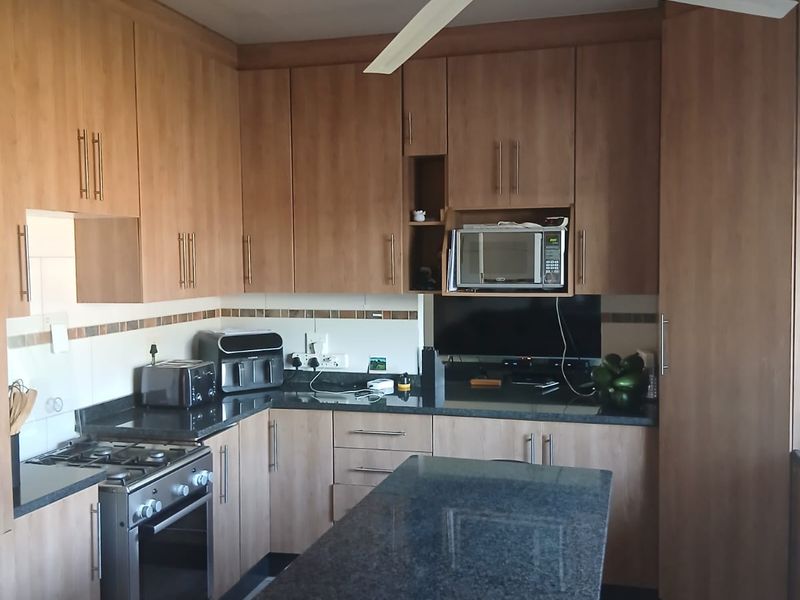 A functional kitchen featuring wood-look laminate cabinetry, granite countertops, a gas stove, and a central island with integrated seating.