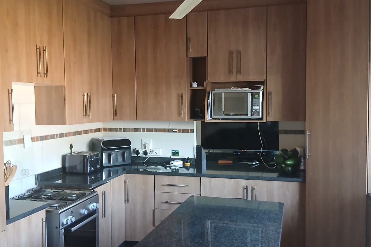 A functional kitchen featuring wood-look laminate cabinetry, granite countertops, a gas stove, and a central island with integrated seating.