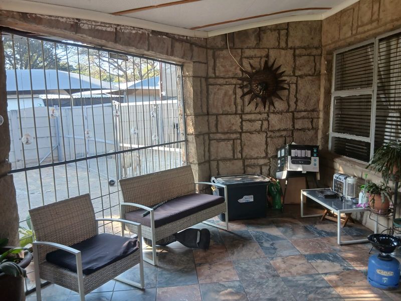 Covered patio area featuring stone-clad walls, tiled flooring, and secure metal screening, offering a functional outdoor space for relaxation.