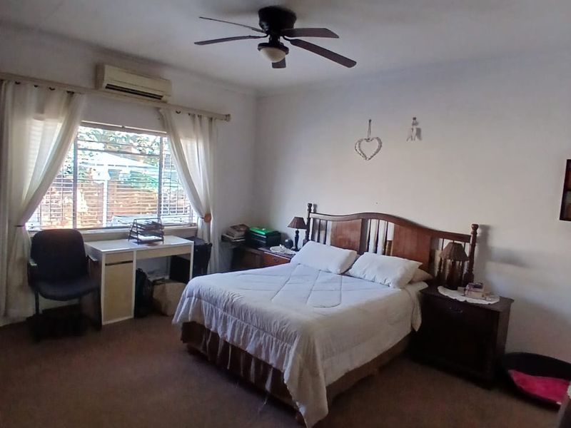 A spacious bedroom featuring a ceiling fan, split-system air conditioning, and carpeted flooring, offering a functional and comfortable living space.