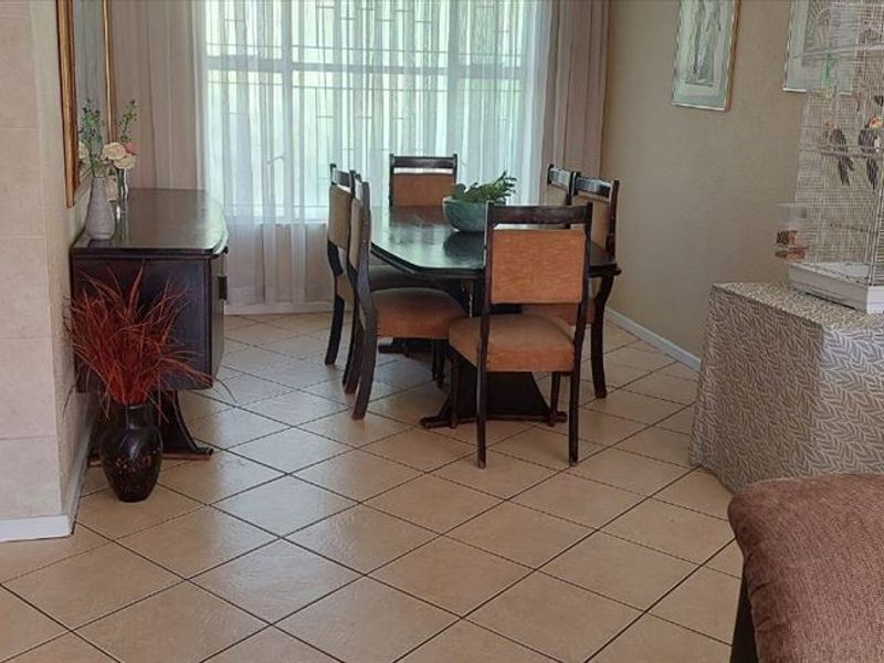 Open plan living and dining area featuring neutral tiled flooring and a large window with security bars, providing natural light to the space.