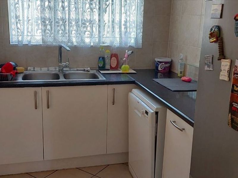 A functional kitchen area featuring built-in cabinetry, a double basin sink with mixer tap, laminate countertops, and tiled splashbacks.