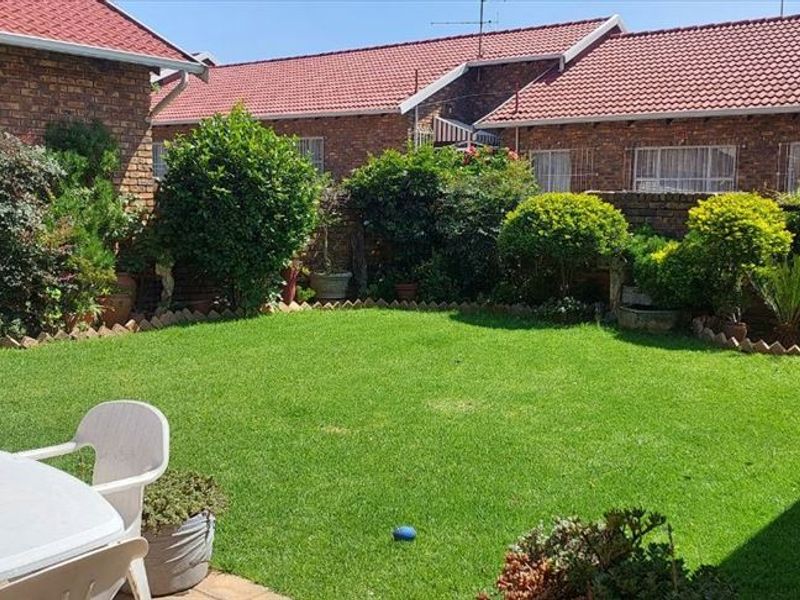 A private rear garden featuring a well-maintained lawn, paved patio area, and brick boundary walls, providing a pleasant outdoor space for the townhouse.