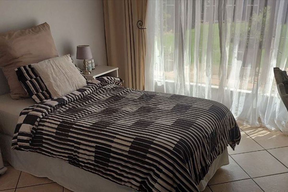 A bedroom featuring tiled flooring and large windows with curtain rails, providing natural light and garden views.