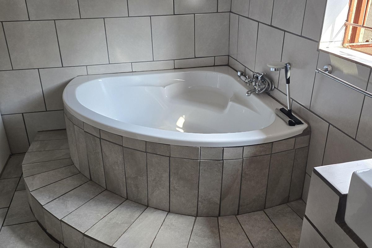 A bathroom featuring a raised corner bathtub with tiled surround and neutral ceramic wall and floor tiling.