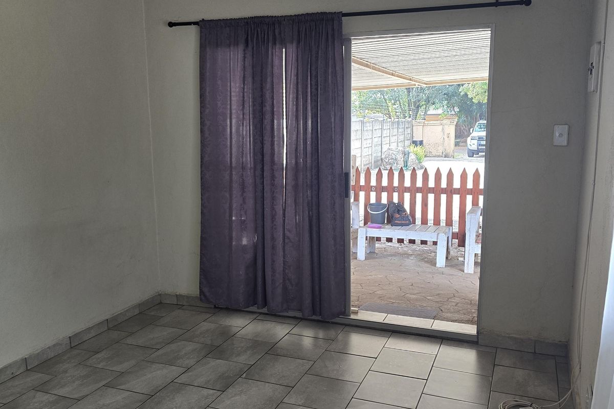 An empty living room featuring grey tiled flooring, a ceiling fan, and a sliding glass door providing access to an outdoor patio area.