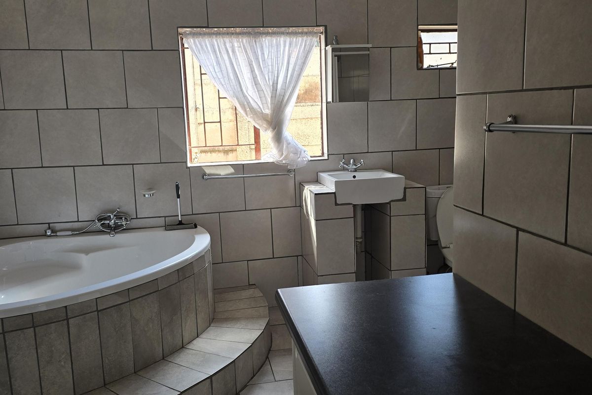 A functional bathroom featuring a raised corner bathtub, tiled vanity with basin, and neutral ceramic wall and floor tiling throughout.