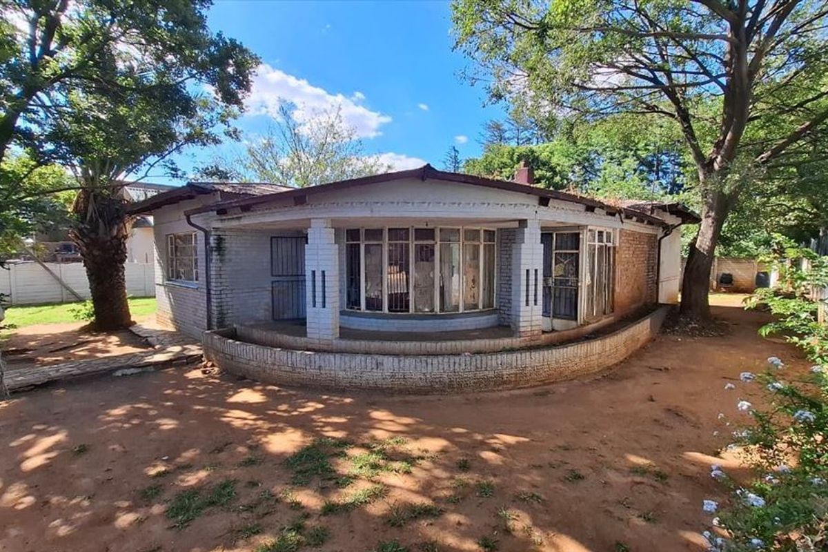 Rear view of a single-story brick house featuring a curved veranda, metal-framed windows, and a large, unlandscaped garden area.