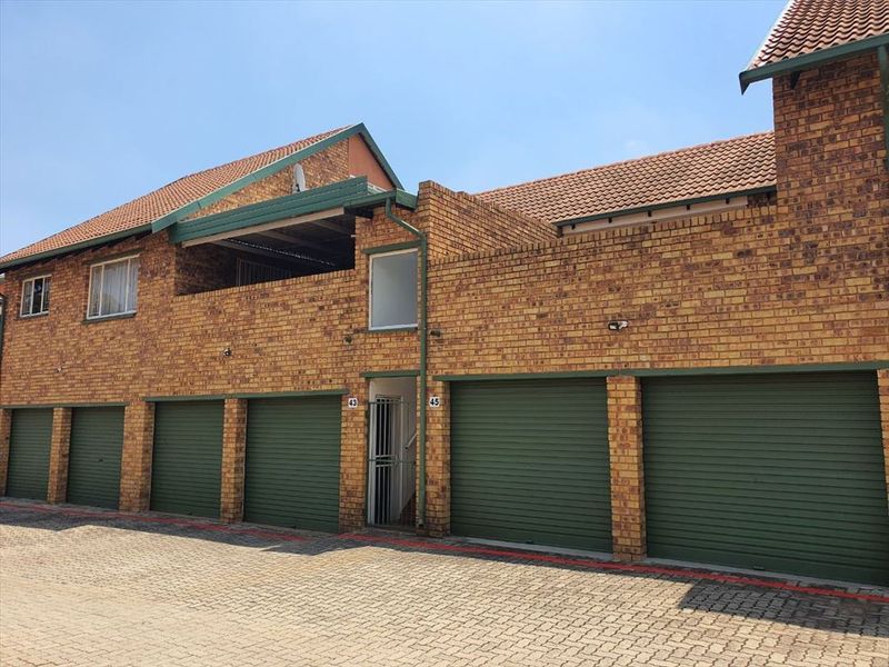 Front elevation of a townhouse complex featuring face brick construction, multiple roller shutter garage doors, and an upper-level balcony.