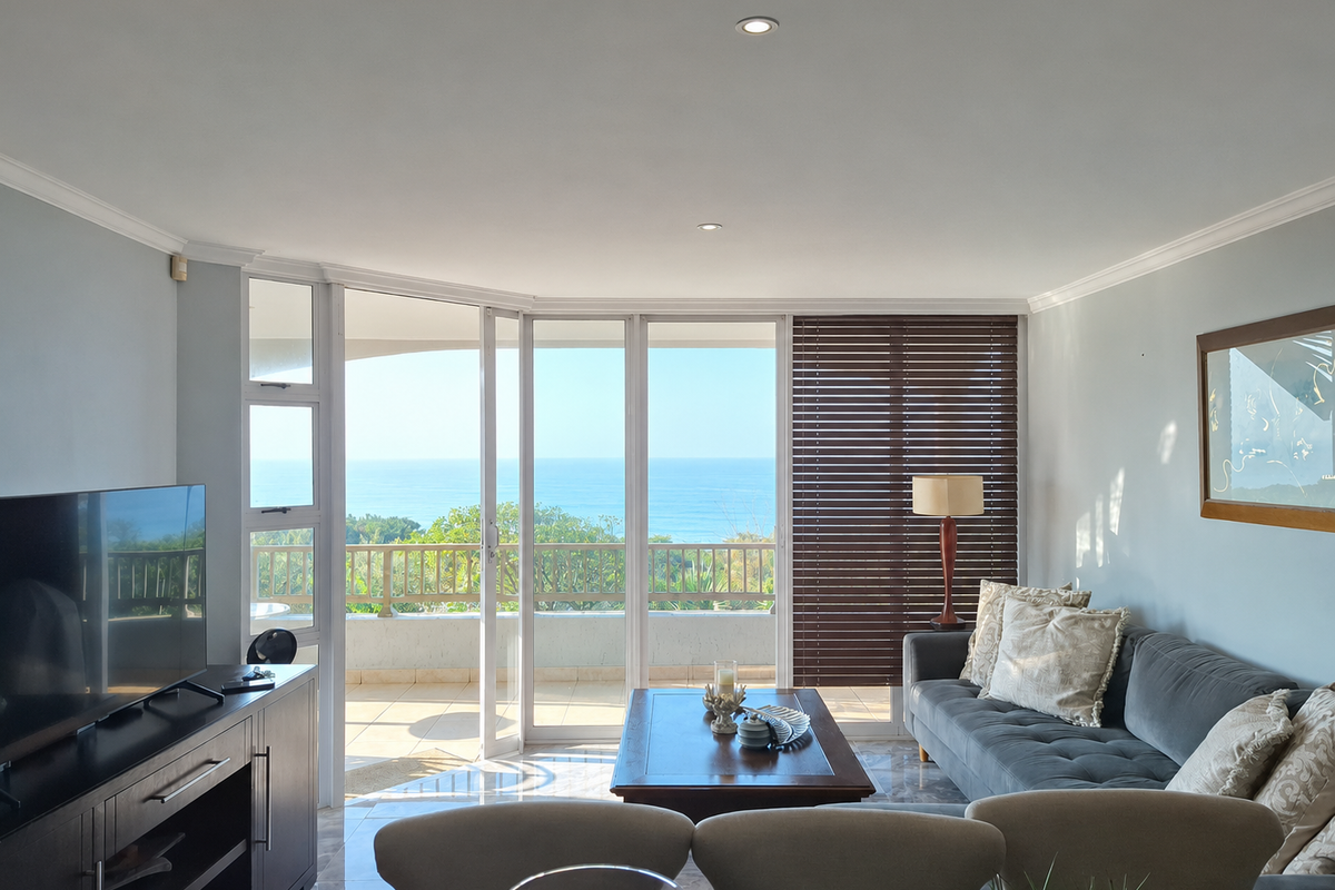 A bright living room featuring tiled flooring, recessed lighting, and large sliding glass doors that open onto a balcony with ocean views.