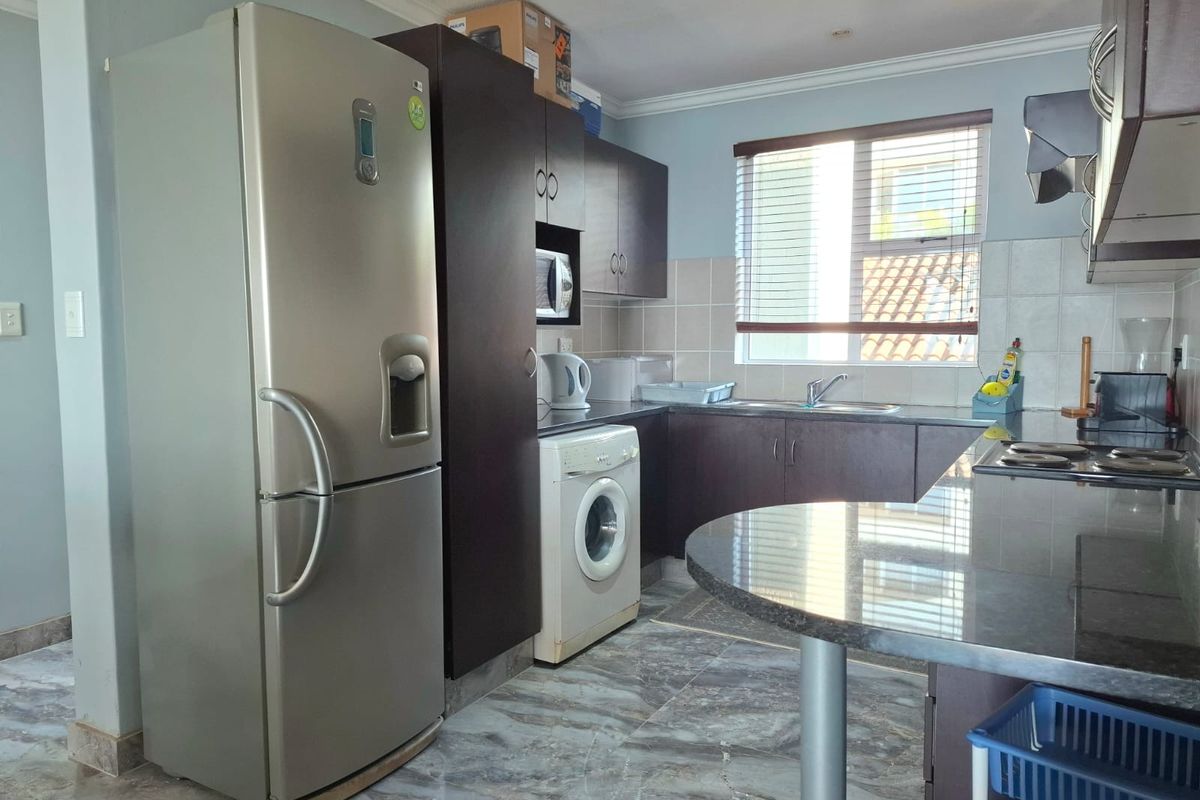 A functional kitchen featuring dark wood cabinetry, granite countertops, tiled backsplash, and integrated appliances, including a hob, oven, and extractor fan.