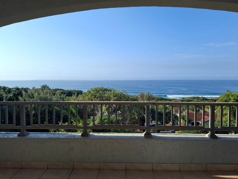A spacious balcony featuring tiled flooring and a balustrade, offering expansive views of the surrounding greenery and the ocean.