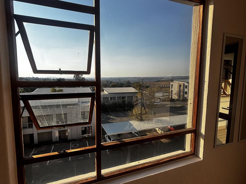 A view from an interior room looking out over a parking area and surrounding neighborhood through a timber-framed window.