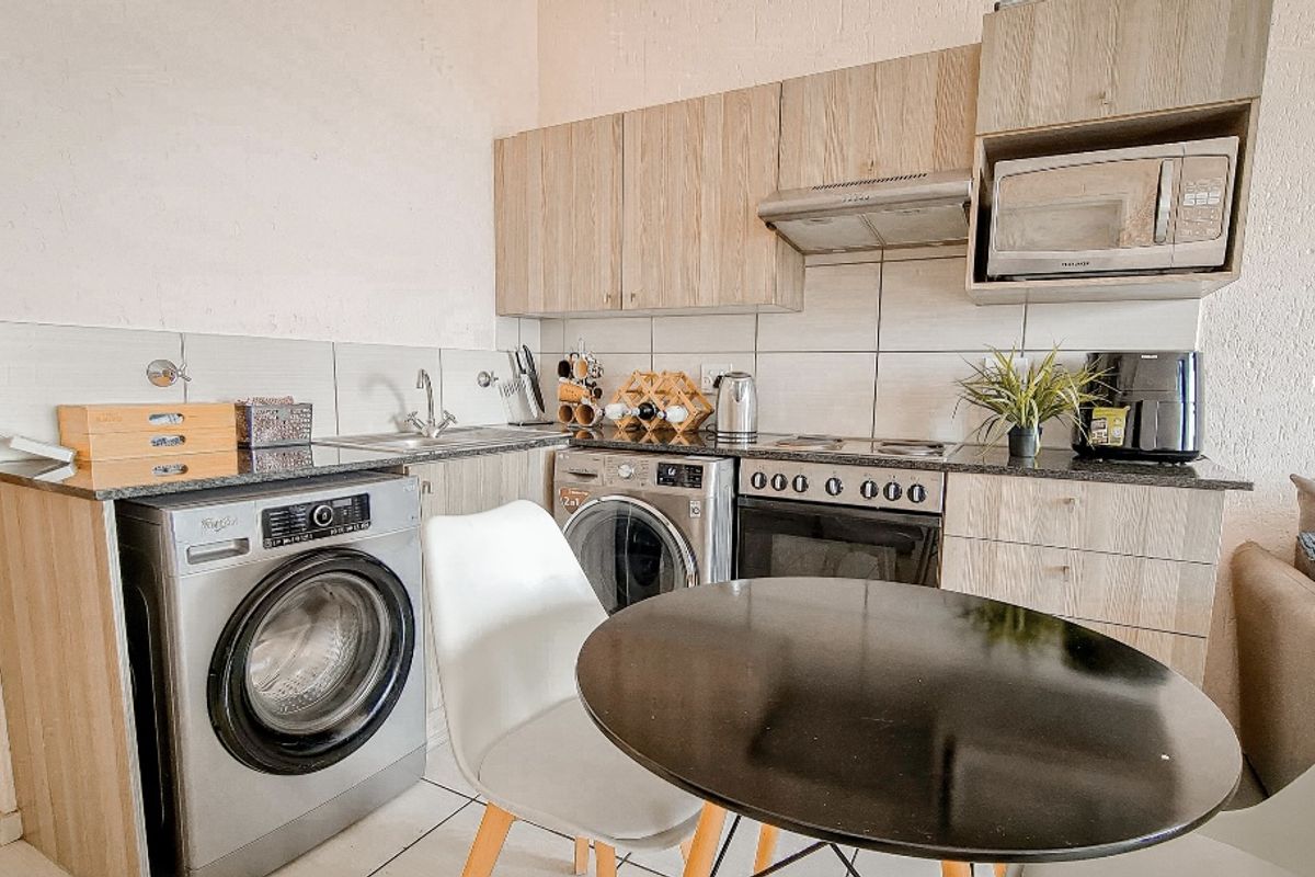 Compact kitchen featuring modern wood-finish cabinetry, granite countertops, integrated appliances, and a tiled backsplash, designed for efficient apartment living.