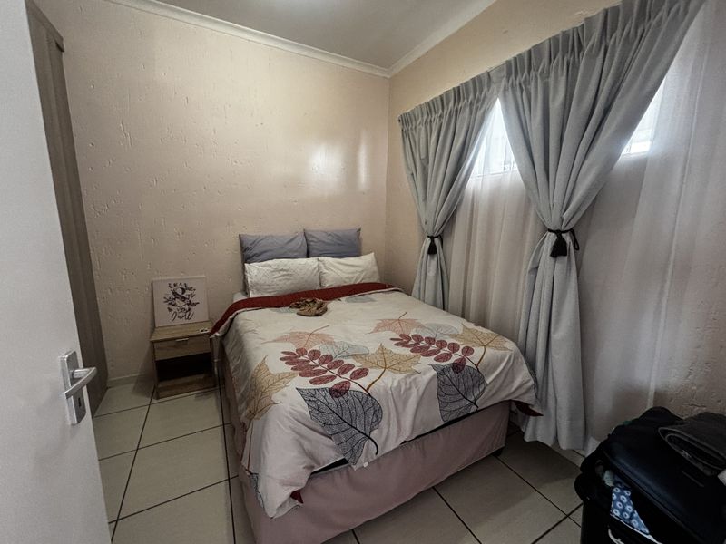 A compact bedroom featuring tiled flooring and a built-in cupboard, providing a functional sleeping space with neutral wall finishes.