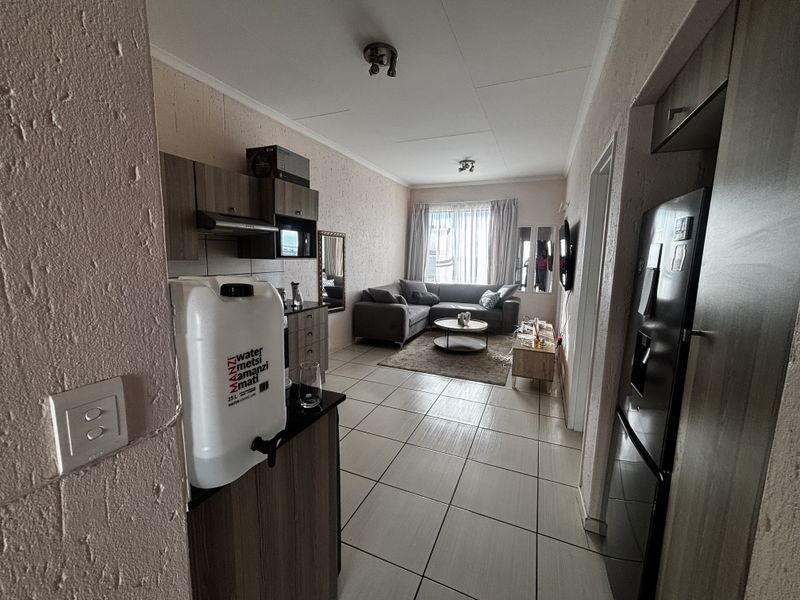 Open-plan living area featuring tiled flooring, built-in kitchen cabinetry with an extractor fan, and direct access to the lounge space.