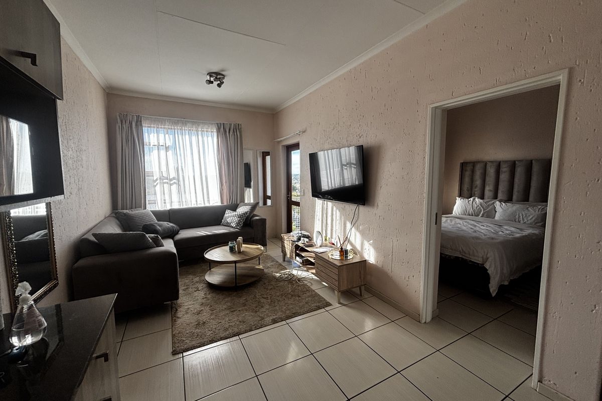 A living room featuring tiled flooring and textured walls, with direct access to an adjacent bedroom and natural light from the balcony door.