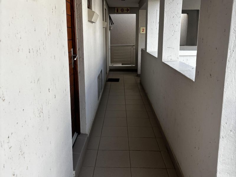A functional apartment hallway featuring tiled flooring and textured walls, providing access to the unit entrance.