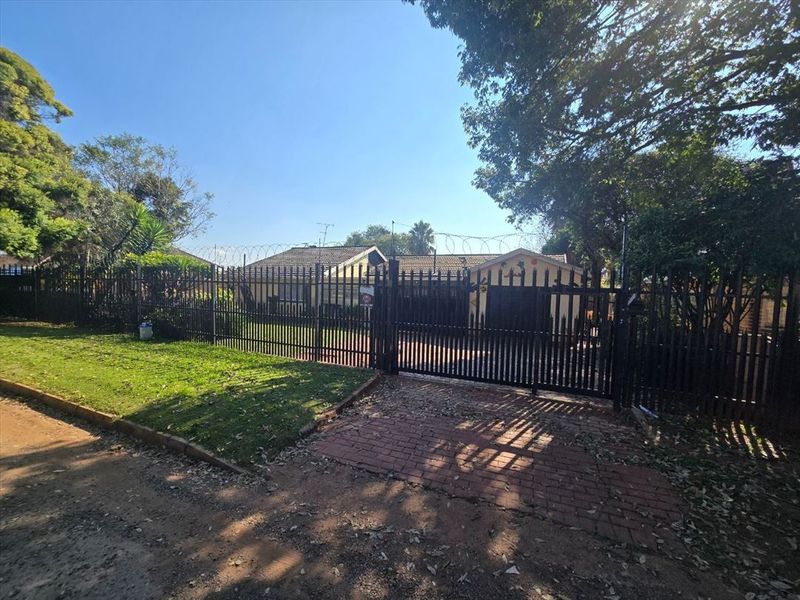 Front view of the property featuring a secure gated entrance, perimeter fencing with razor wire, and a paved driveway leading to the house.