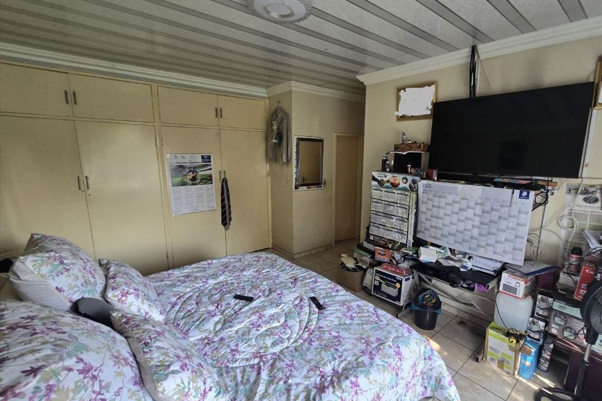 A bedroom featuring built-in cupboards, tiled flooring, and a panelled ceiling, offering a functional space with potential for cosmetic updates.