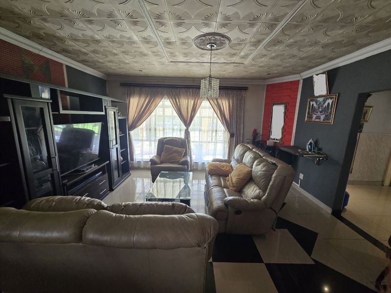 A living room featuring tiled flooring, decorative ceiling tiles, and a ceiling rose, with access to the outdoors via a sliding glass door.
