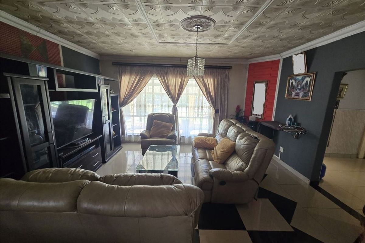 A living room featuring tiled flooring, decorative ceiling tiles, and a ceiling rose, with access to the outdoors via a sliding glass door.
