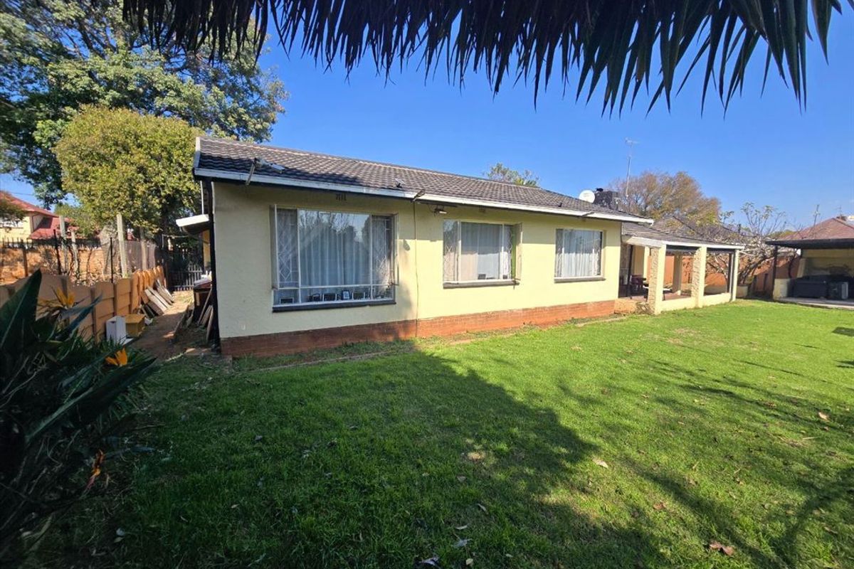Rear view of the house featuring a tiled roof, plastered exterior walls, and a covered patio area overlooking the garden.